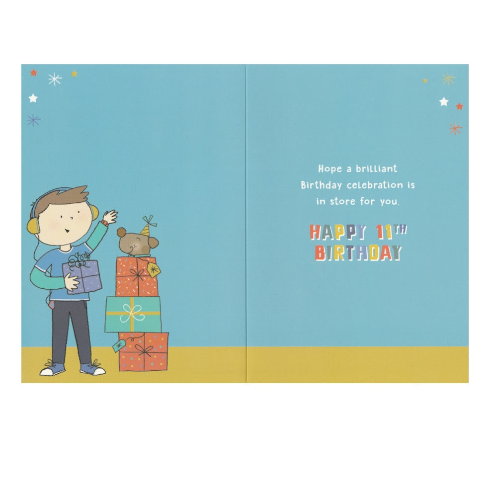 Front of this 11th birthday card features an illustration of boy standing near a stack of presents, paired with a message.