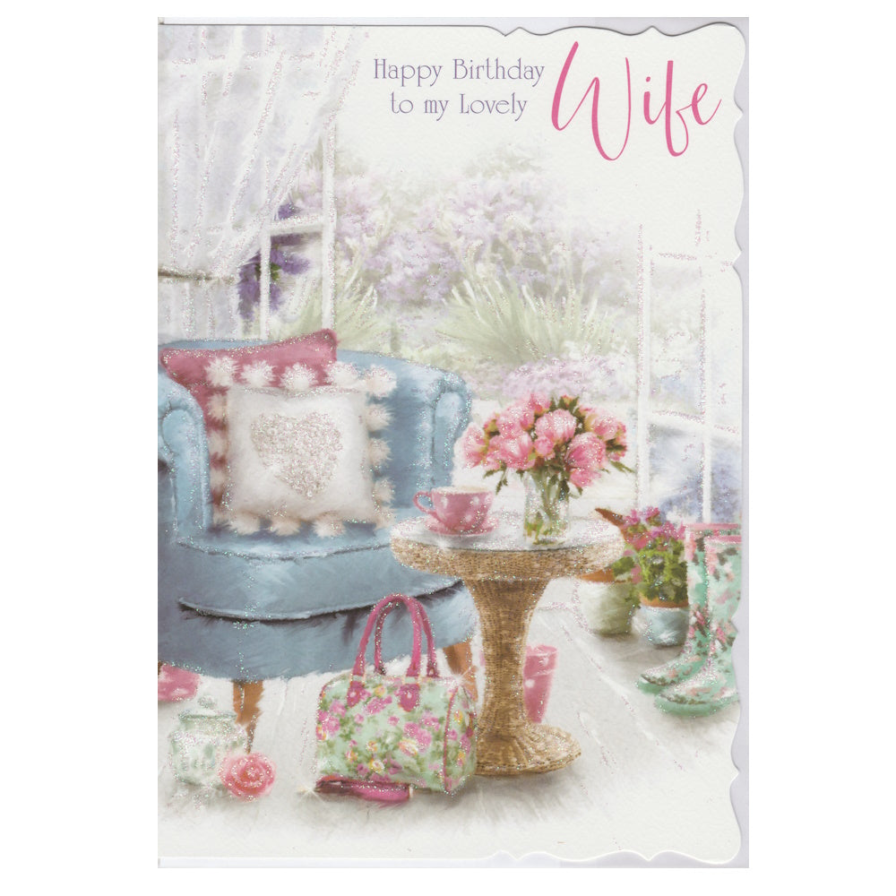 Front of this wife birthday card features an illustration of a sunroom scene with a blue armchair, table and flowers, paired with a message.